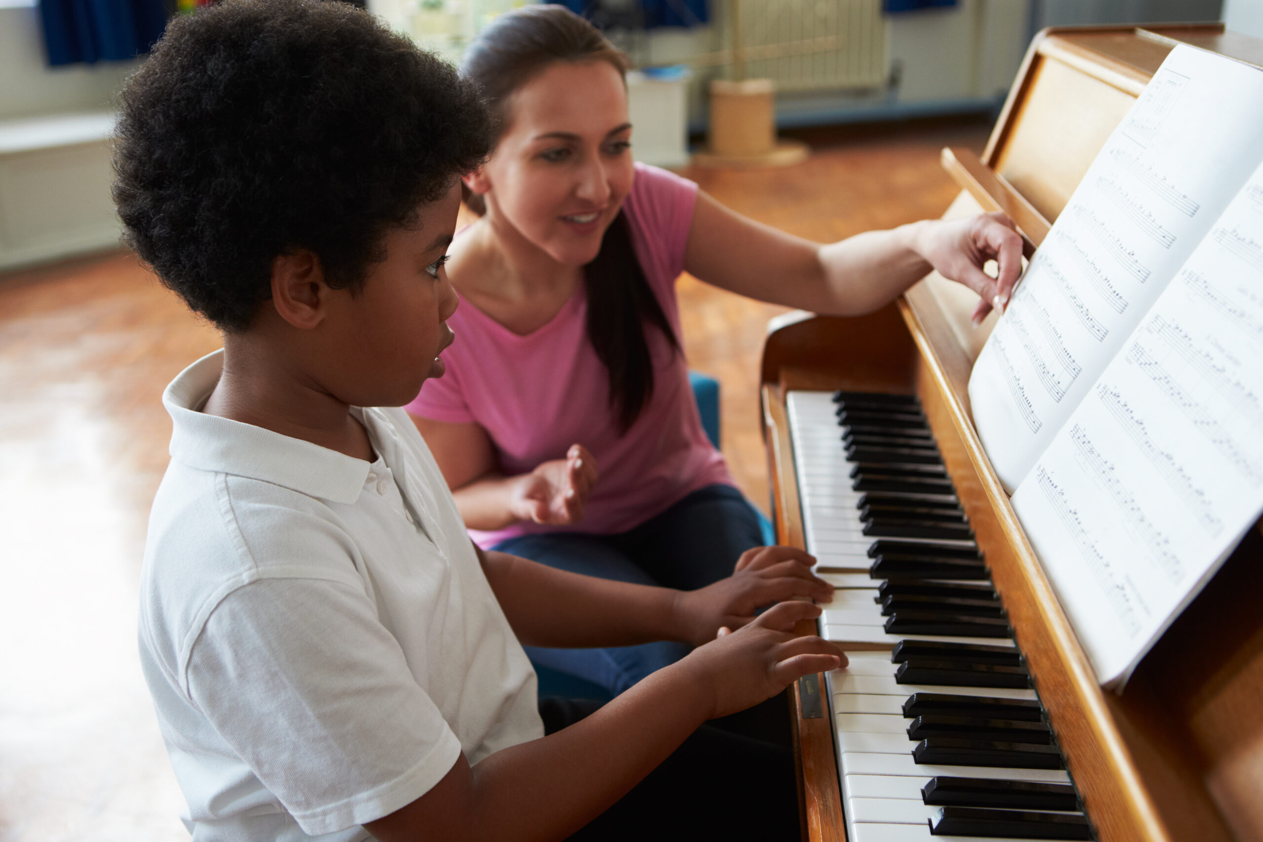A photo of a female adult teaching a student, aged between 5 and 7, to play piano.